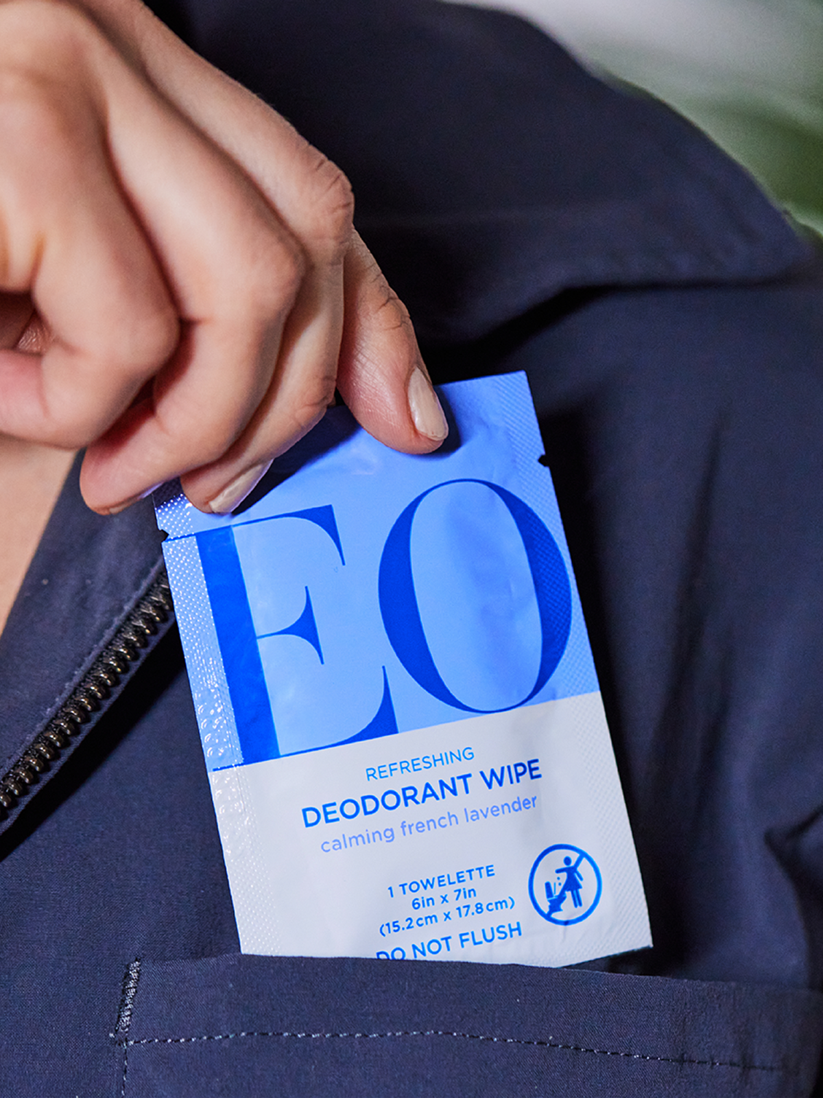 Hand holding an EO deodorant wipe against a dark jacket background