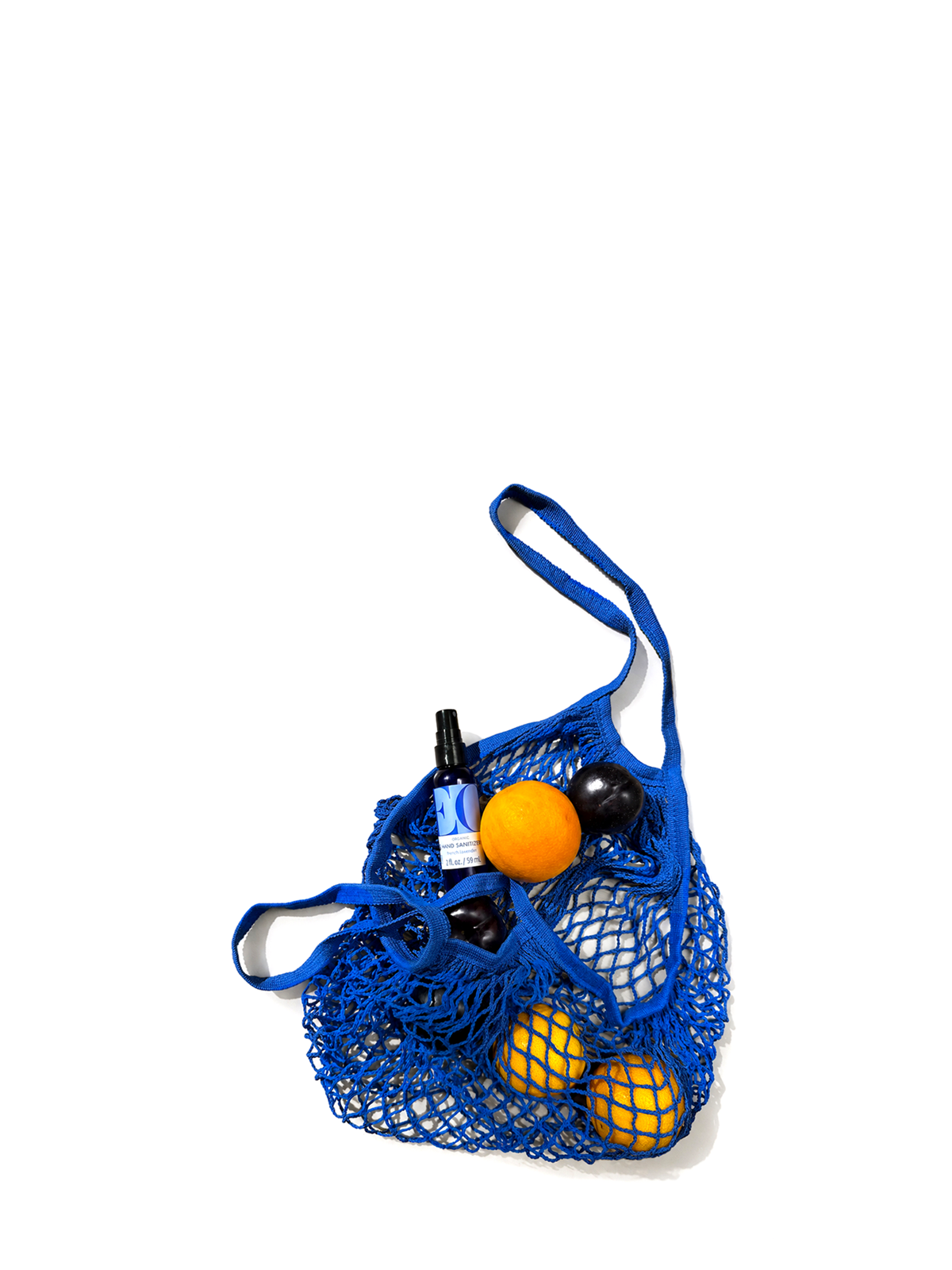 A blue mesh shopping bag with shoulder straps, filled with fruit and a small sanitizer bottle, photographed on a clean white background.